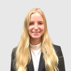 Professionele jonge vrouw met lang blond haar, gekleed in een zwarte blazer en witte top, poseert glimlachend voor een neutrale achtergrond.